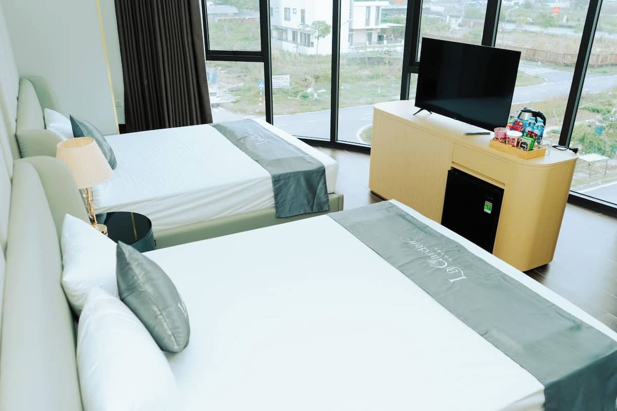 A hotel room with two beds, a TV, a minibar, and a view of the outside.