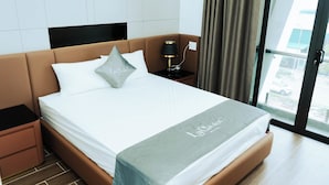 Une chambre d’hôtel moderne avec un grand lit, une table de chevet, une lampe et une vue sur l’extérieur grâce à une grande fenêtre.