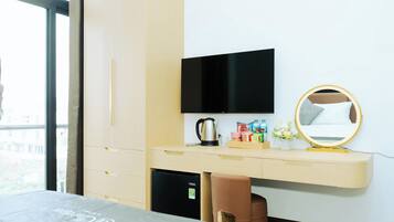 Habitación de hotel con cama, escritorio con televisor de pantalla plana, cafetera, artículos de aseo y un espejo pequeño.