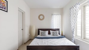 A bedroom with a bed, a bedside lamp, a wall mirror, and a window with curtains. - Aira Luxe by Red Olivebyg Brewskiwifi (Bengaluru)