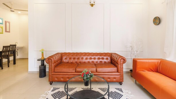 A living room with a brown leather sofa, a glass coffee table with flowers, and a dining area with a wooden table and chairs. - Aira Luxe by Red Olivebyg Brewskiwifi (Bengaluru)