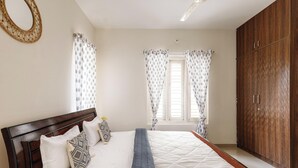A bedroom with a wooden headboard, a bed with patterned pillows, a quilted bedspread, and a wardrobe. - Aira Luxe by Red Olivebyg Brewskiwifi (Bengaluru)