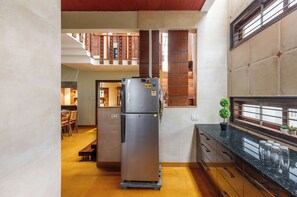 A compact kitchen with a refrigerator, wooden cabinets, and a dining area with chairs. - Terrastone Duplex Apartment (Bengaluru)