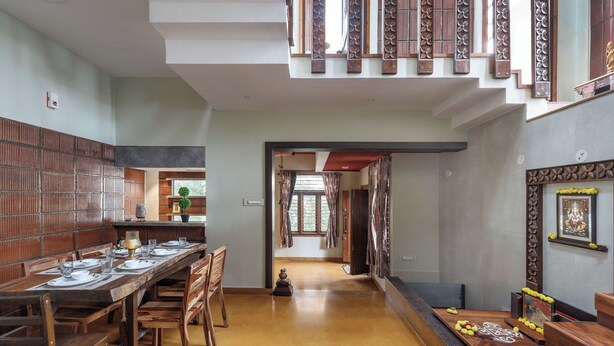 A spacious dining area with a long wooden table set for a meal, a staircase with decorative railings, and a view of the adjacent room.