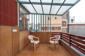 A balcony with two chairs, a wooden wall, and a view of neighboring buildings.