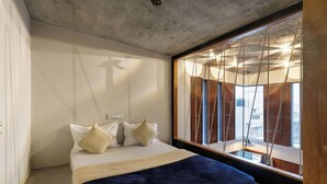 A bedroom with a bed, pillows, a wooden headboard, and a large window with curtains.