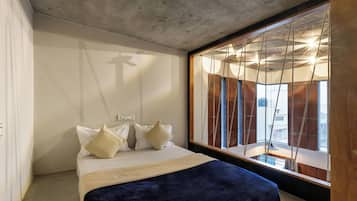 A bedroom with a bed, pillows, a wooden headboard, and a large window with curtains.