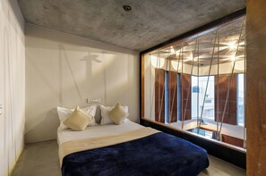 A bedroom with a bed, pillows, a wooden headboard, and a large window with curtains.