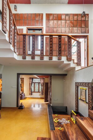 A spacious interior with a wooden staircase, a high ceiling, and a view of the outdoors. - Terrastone Duplex Apartment (Bengaluru)