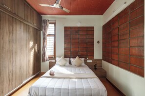 A bedroom with a bed, wooden wardrobe, ceiling fan, and a window with curtains. - Terrastone Duplex Apartment (Bengaluru)