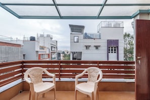 A balcony with two white plastic chairs, a wooden door, and a view of buildings in the background.