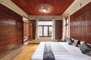 A bedroom with a large bed, wooden sliding doors, a ceiling fan, and a window with curtains.