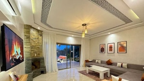 A modern living room with a stone fireplace, a large flat-screen TV, a sofa set, and a coffee table. - villa ssekan (Oulad Hassoune)