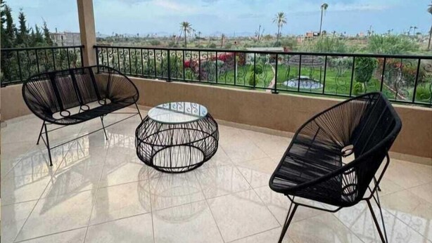 A covered outdoor area with two black wireframe chairs and a round table, a tiled floor, and a view of a distant landscape. - villa ssekan (Oulad Hassoune)