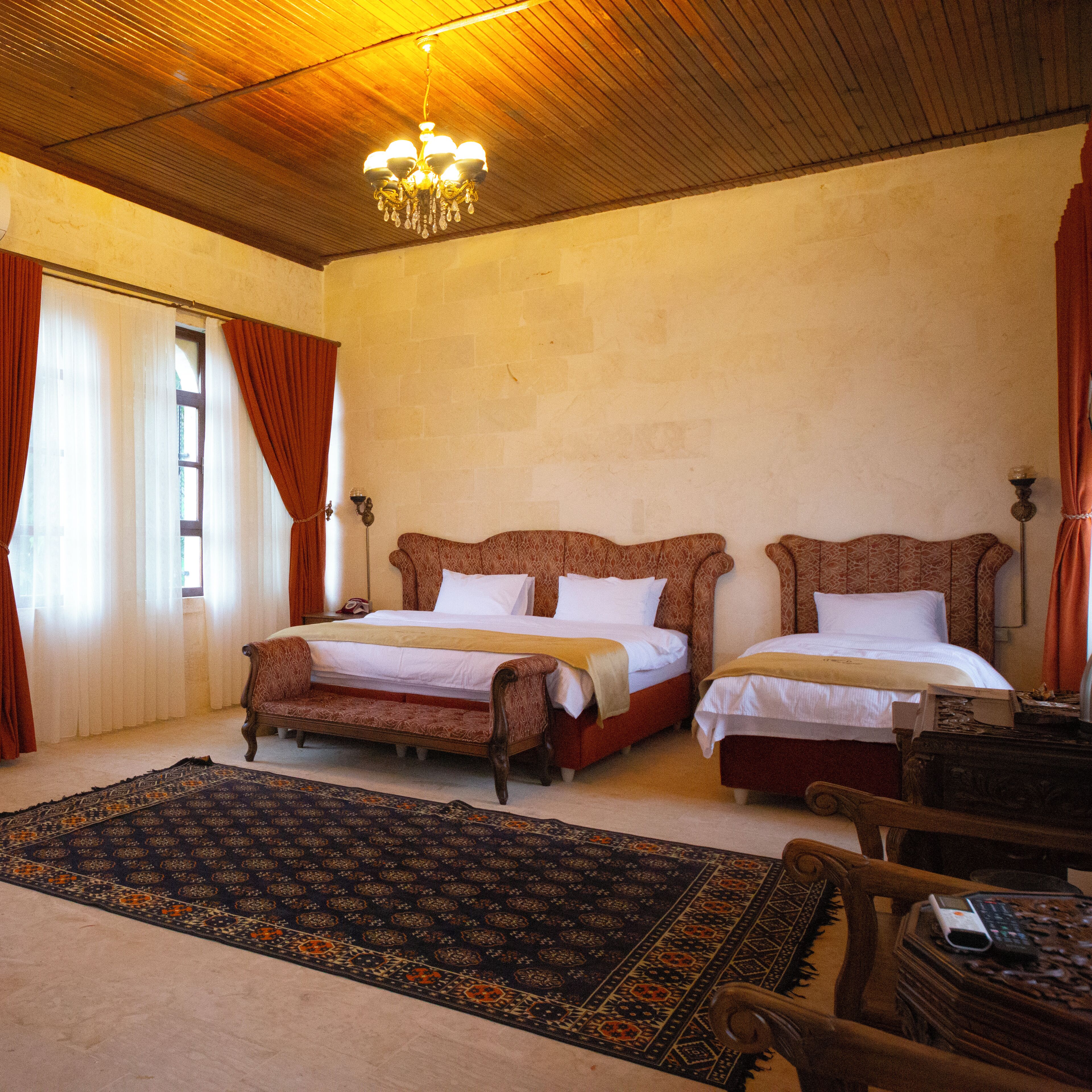 Habitación de hotel con dos camas, un candelabro, una alfombra estampada y techo de madera.