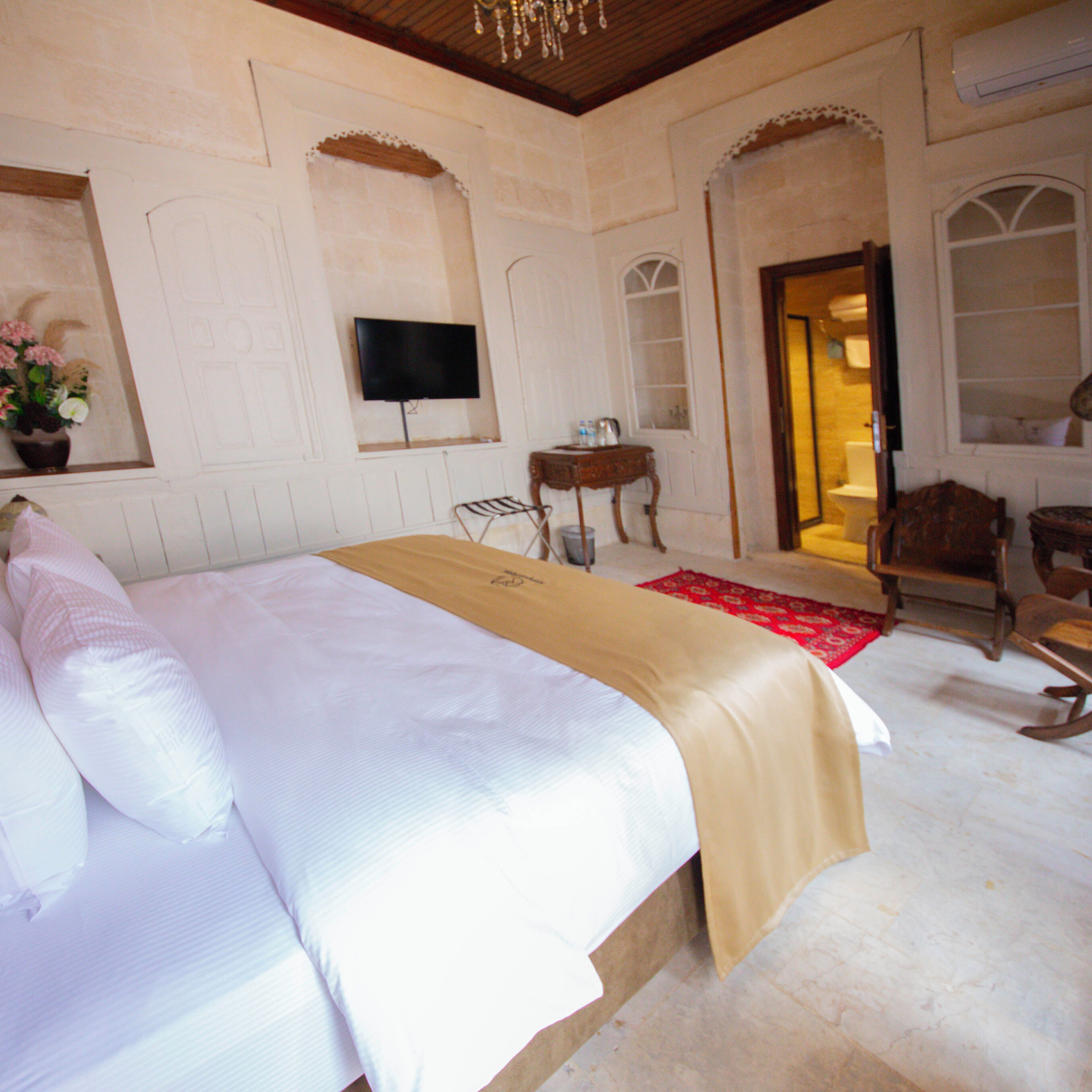 A bedroom with a large bed, a television mounted on the wall, a small table, and a chair.