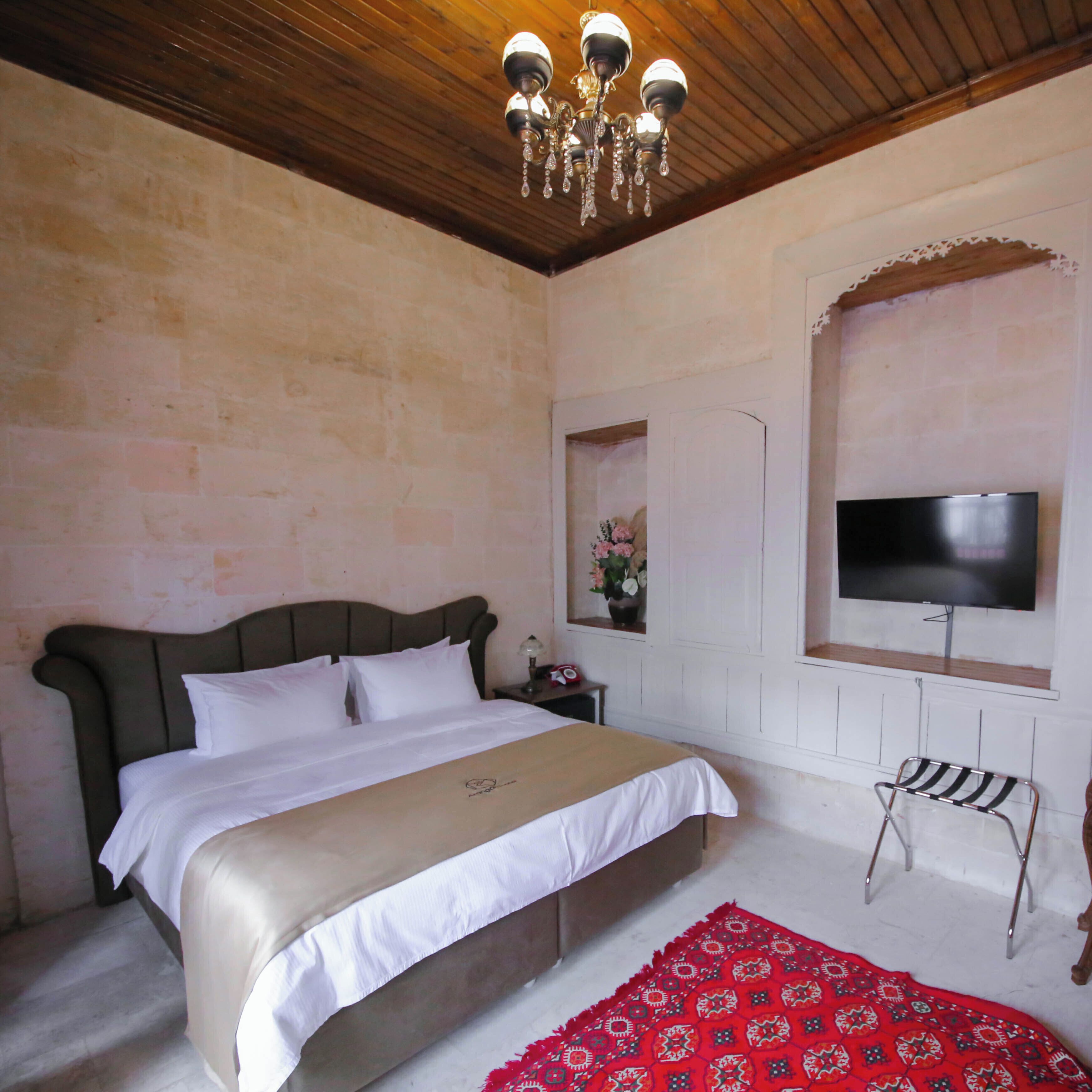 Ein Schlafzimmer mit Bett, Fernseher, Fenster und einer Chandelier.