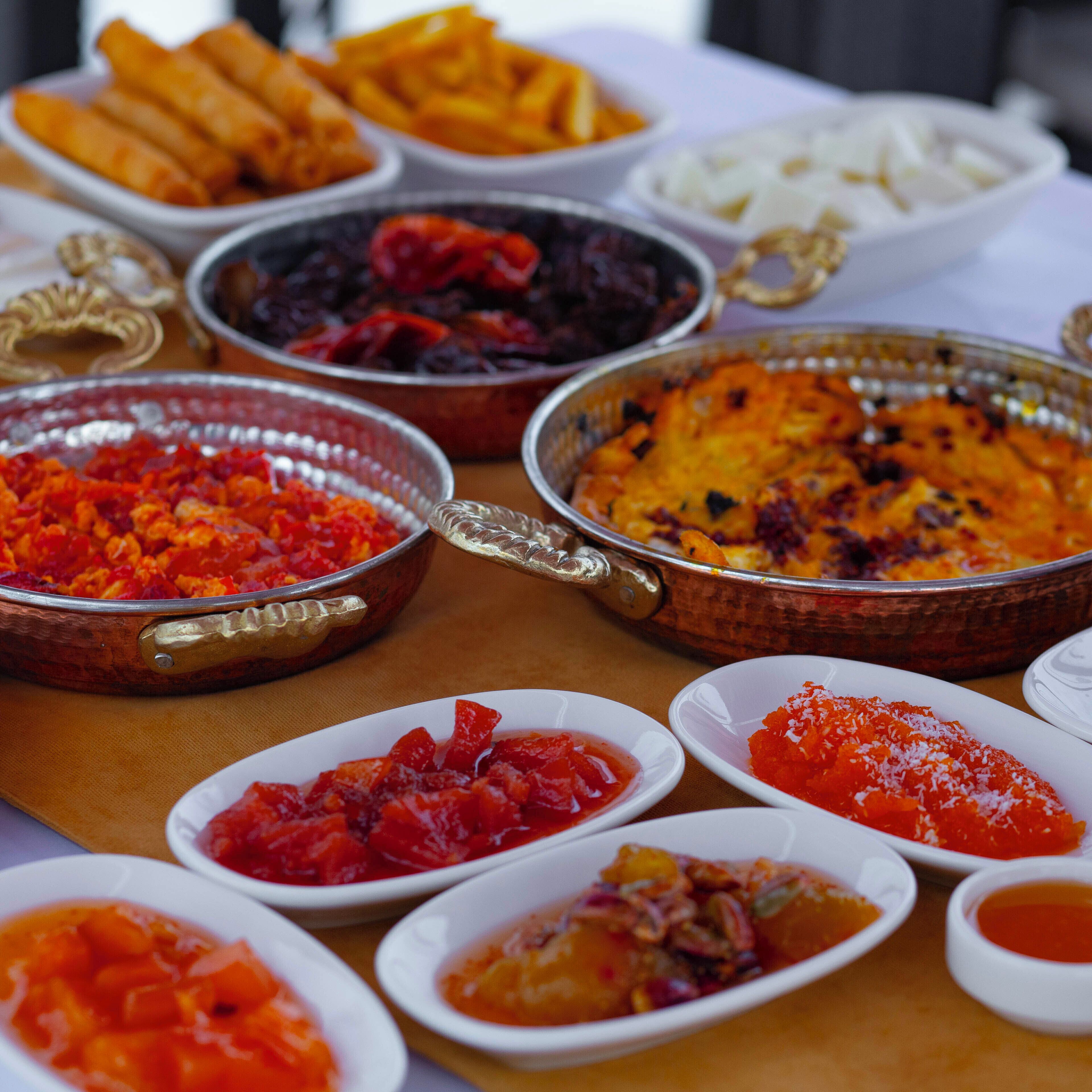 Variedad de platos sobre una mesa, incluyendo una olla de cobre grande con asa, varios recipientes pequeños blancos y un plato con alimentos fritos.