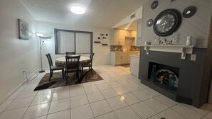 A modern kitchen with a dining area, featuring a fireplace, a clock, and a kitchen island.