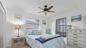 A bedroom with a bed, a nightstand, a dresser, a ceiling fan, and artwork on the walls.
