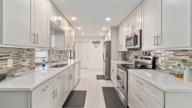 A modern kitchen with white cabinets, stainless steel appliances, and a tiled backsplash.