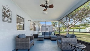 A covered patio area with wicker furniture, a ceiling fan, and a view of the backyard.