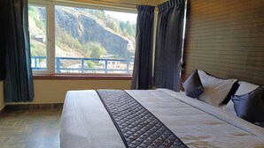 A bedroom with a large bed, a view of a mountainous landscape through a window, and a wooden headboard.