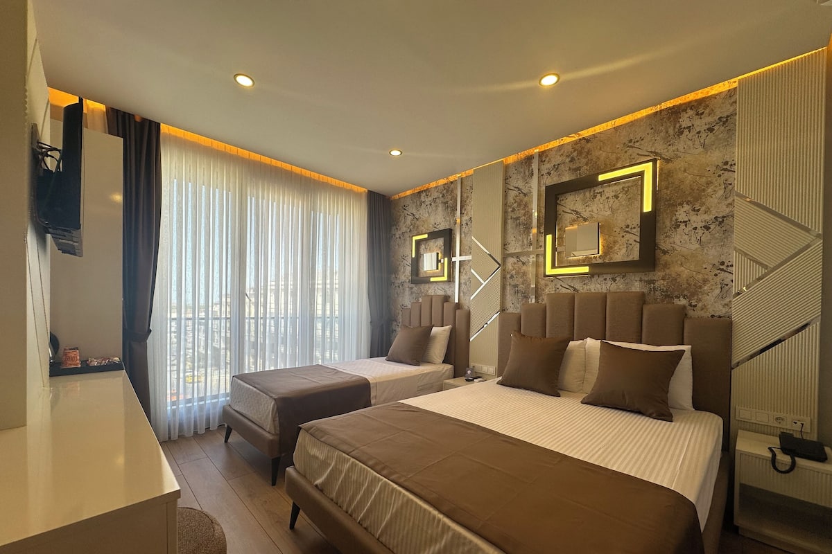 A modern hotel room with a large bed, a smaller bed, a desk, and a chair.