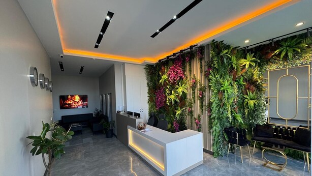 Un espace d’accueil moderne avec un comptoir de réception blanc, un grand mur végétal et un coin salon avec des chaises noires et un canapé noir.