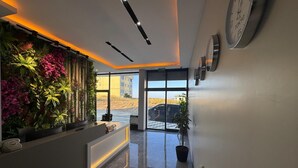 Et moderne receptionområde med en blomstervæg, et receptionistskranke og et ur på væggen.