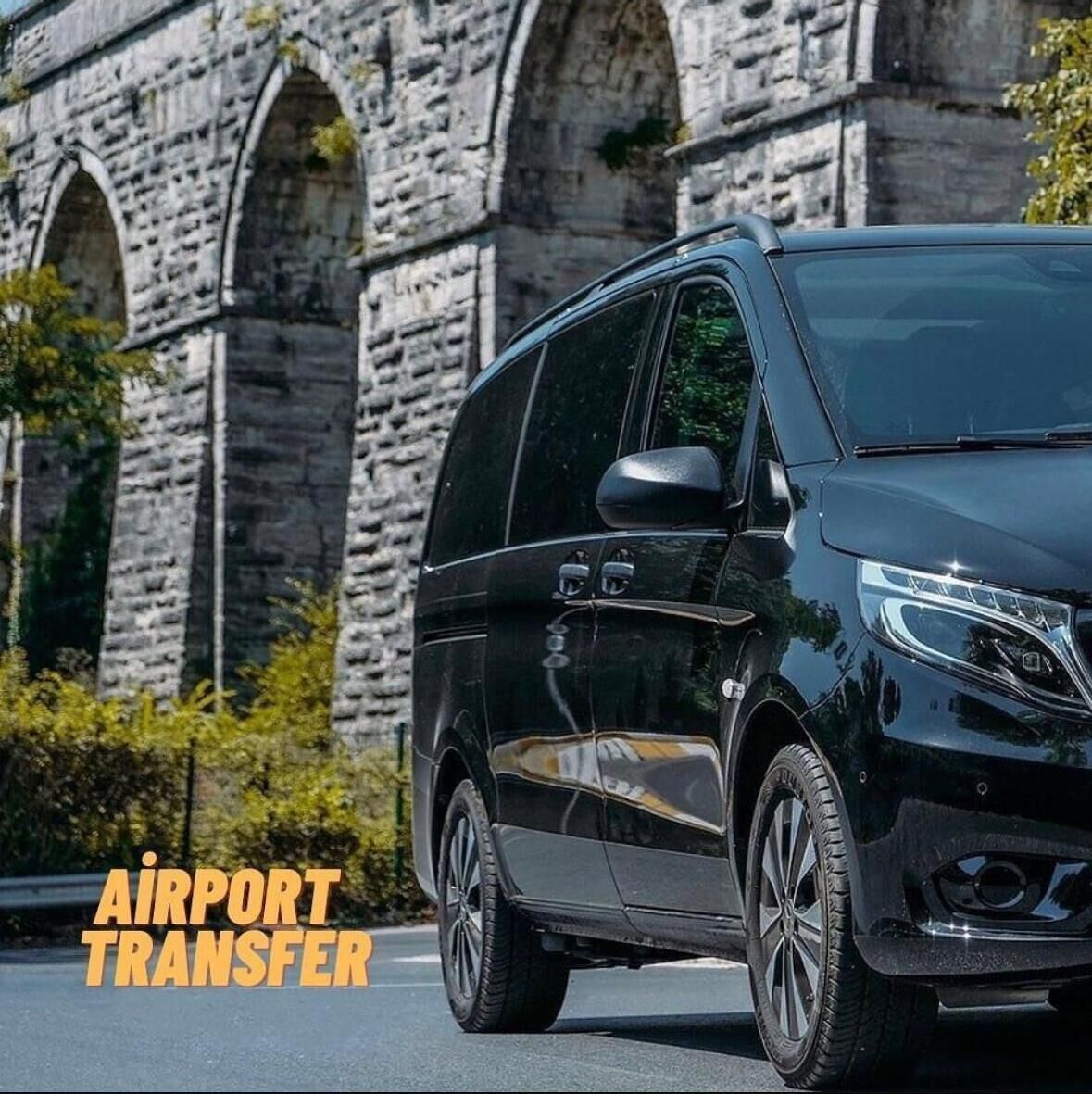 A black minivan parked in front of a stone building with arched windows.