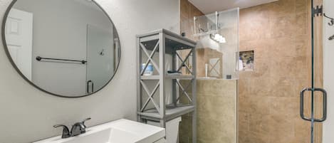 A bathroom with a white sink, a round mirror, a glass-enclosed shower, and a toilet.