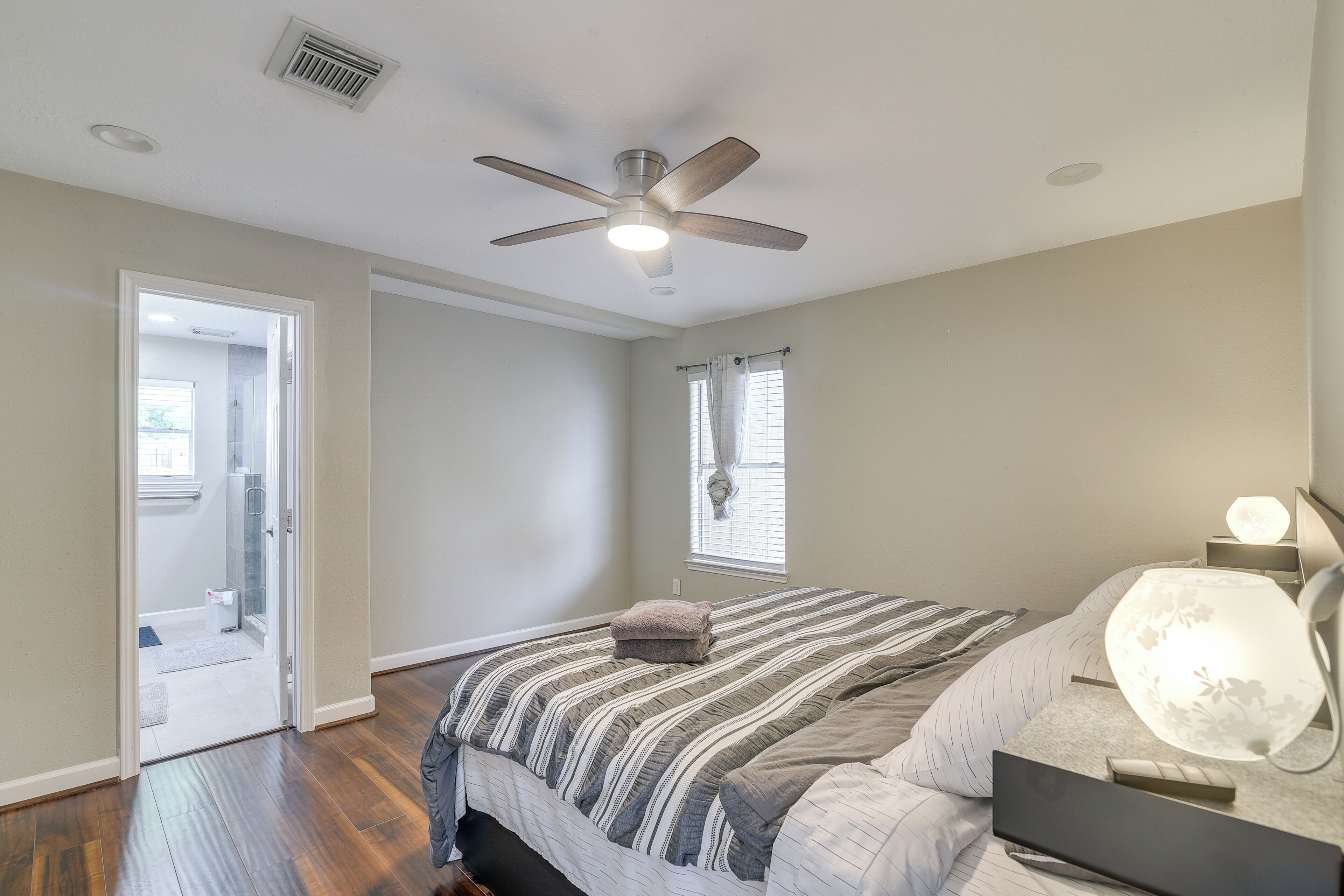 Ein Schlafzimmer mit einem Bett, einem Deckenventilator, einer Nachttischlampe und einem Fenster mit Vorhängen.