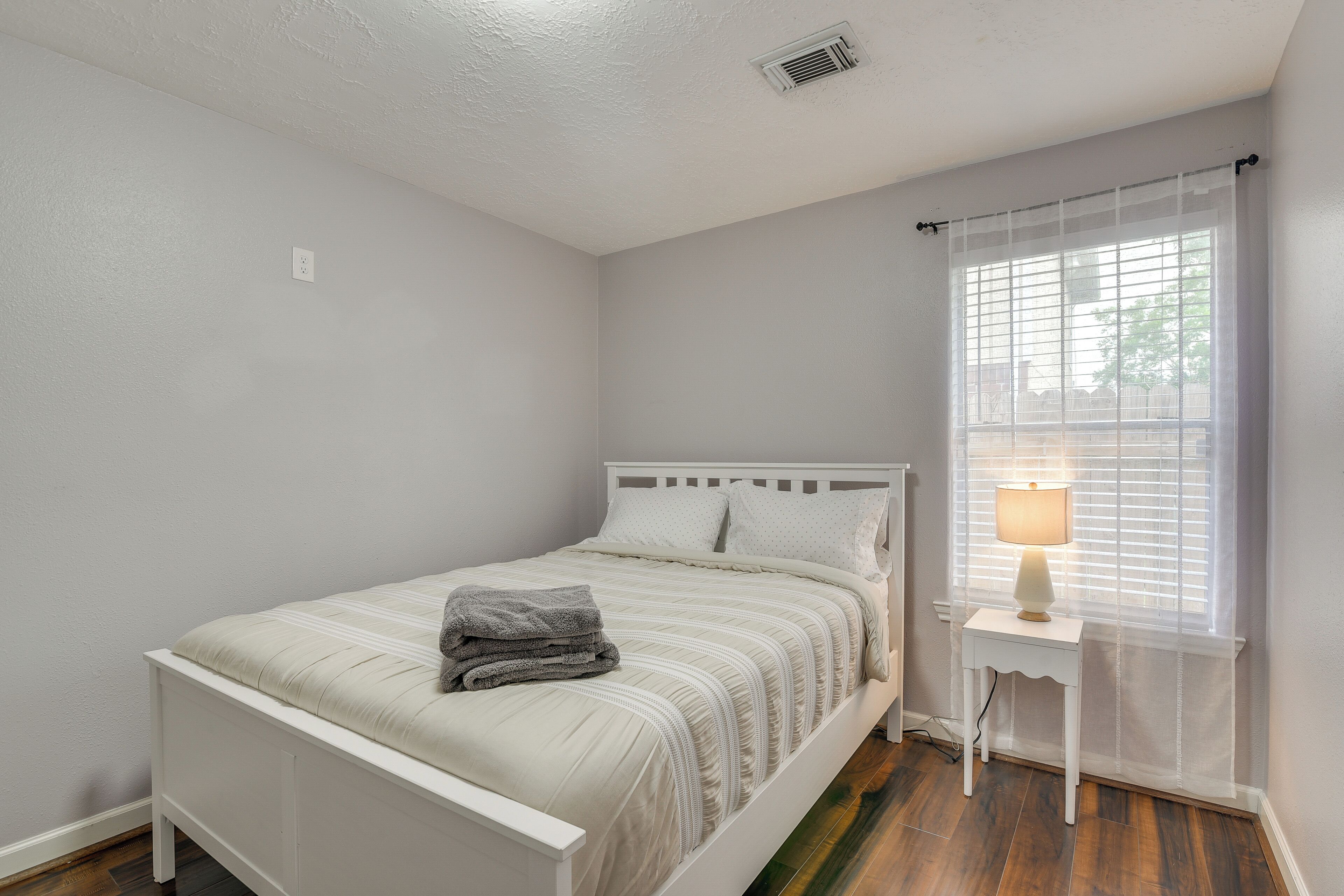 A bedroom with a bed, a bedside table with a lamp, and a window with blinds.