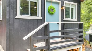 A two-story cabin with a wooden exterior, a front porch with a railing, and a green wreath on the door. - Hike & Fish: Mountain Getaway in Avery! (Avery)