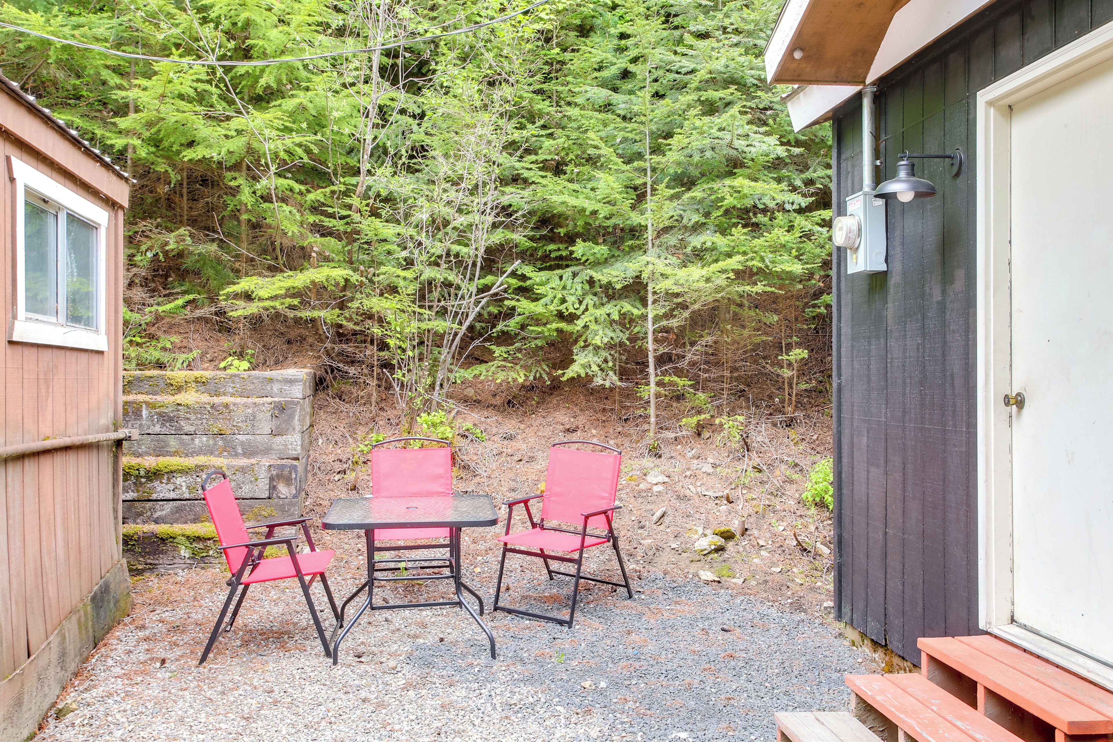 A small outdoor seating area with a table and two chairs, a wooden bench, and a door to a building.