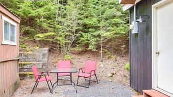 A small outdoor seating area with a table and two chairs, a wooden bench, and a door to a building.