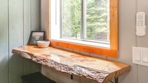 A rustic wooden bench with a unique, textured surface, positioned under a window with a view of a forest. - Hike & Fish: Mountain Getaway in Avery! (Avery)