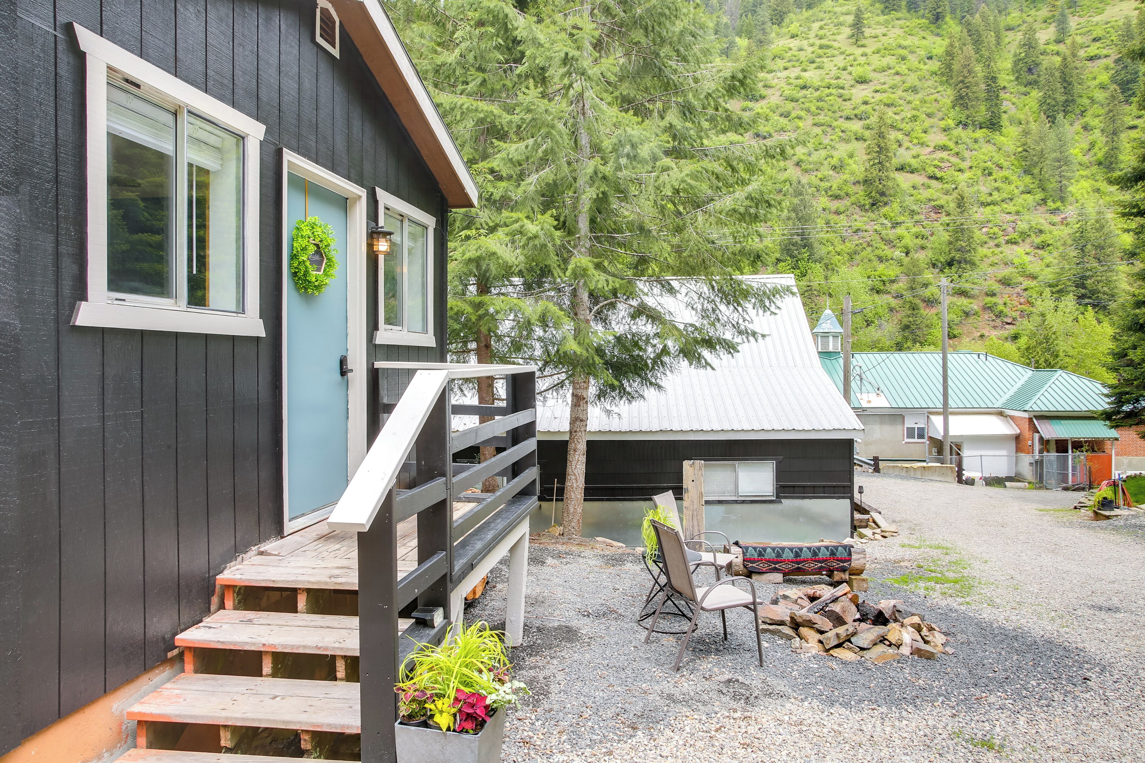A cabin with a wooden deck, a small outdoor seating area, and a view of a forested hillside.