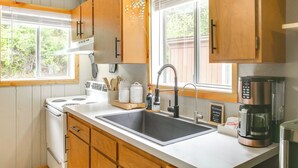 A kitchen with wooden cabinets, a white stove, a sink, and a coffee maker. - Hike & Fish: Mountain Getaway in Avery! (Avery)
