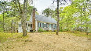 A rustic wooden house with a porch, surrounded by trees and a dirt path. - 1/2 Mi to Cooks Brook Beach: Cape Cod Gem w/ Deck (Eastham)