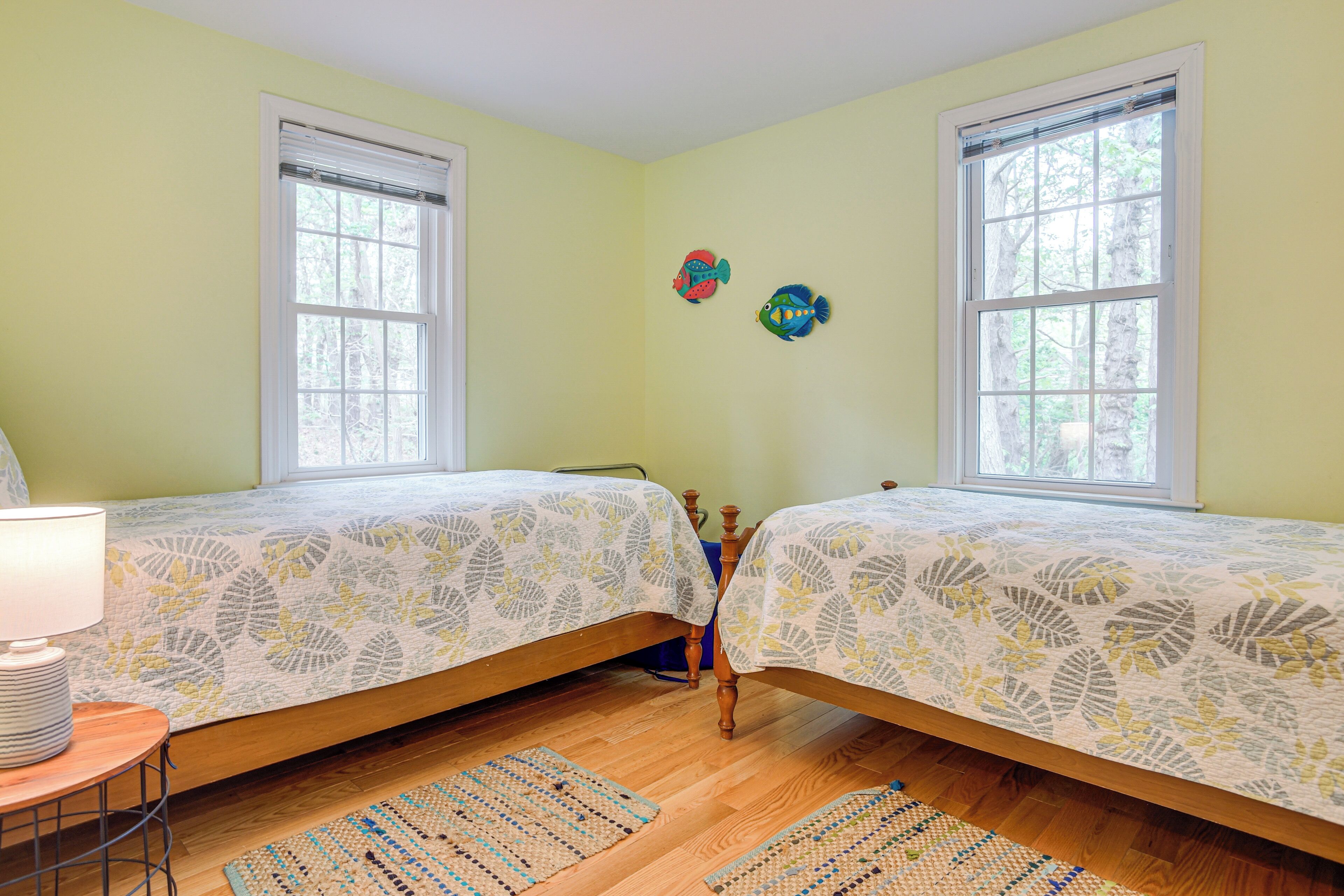 A bedroom with two beds, a bedside table with a lamp, and a window.