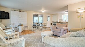 A spacious living area with a white brick accent wall, a dining table with chairs, a sofa, and a flat-screen TV mounted on the wall. - 1/2 Mi to Cooks Brook Beach: Cape Cod Gem w/ Deck (Eastham)