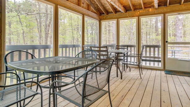 A covered outdoor area with a wooden deck, metal tables and chairs, and large windows offering a view of a forested area. - 1/2 Mi to Cooks Brook Beach: Cape Cod Gem w/ Deck (Eastham)