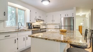 A modern kitchen with white cabinets, granite countertops, stainless steel appliances, and a large island. - 1/2 Mi to Cooks Brook Beach: Cape Cod Gem w/ Deck (Eastham)