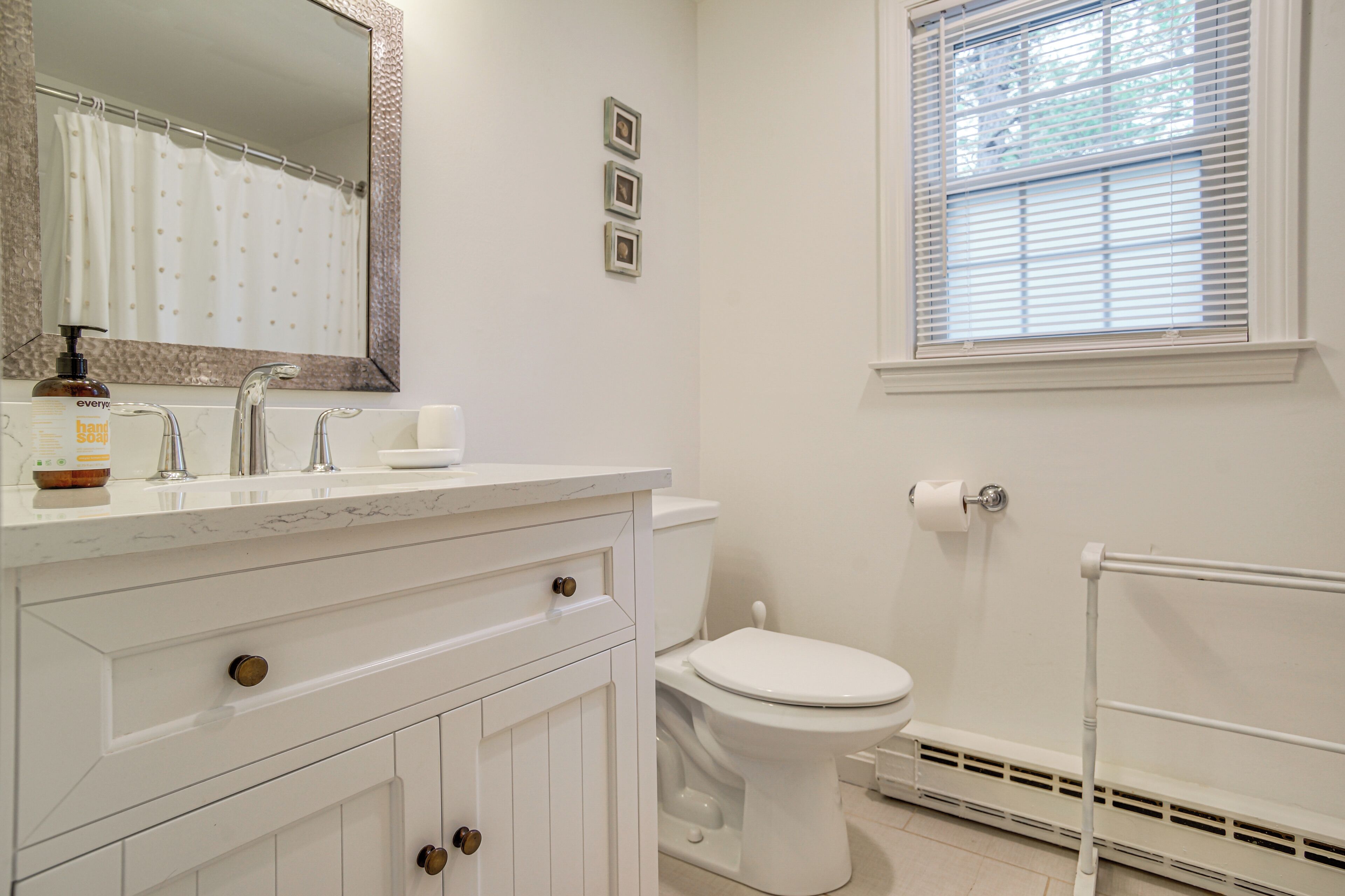 Un bagno con lavandino bianco, specchio, servizi igienici e finestra con persiane.
