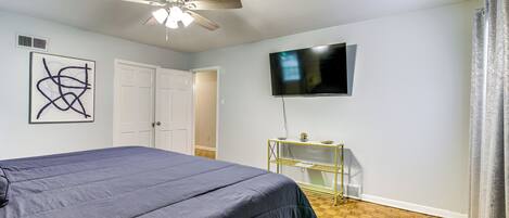 A bedroom with a bed, a ceiling fan, a TV, and a wooden floor.