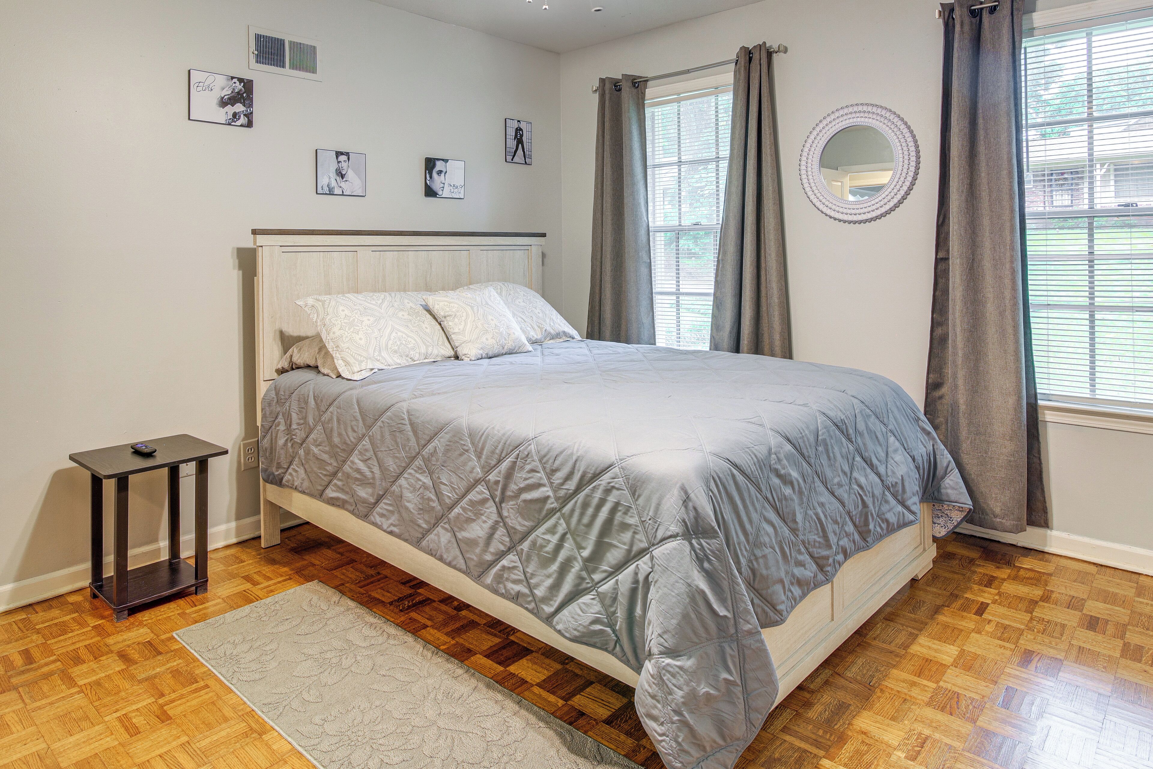 Un dormitorio con cama, una mesita de noche, un tapete, una ventana con cortinas y cuadros en la pared.