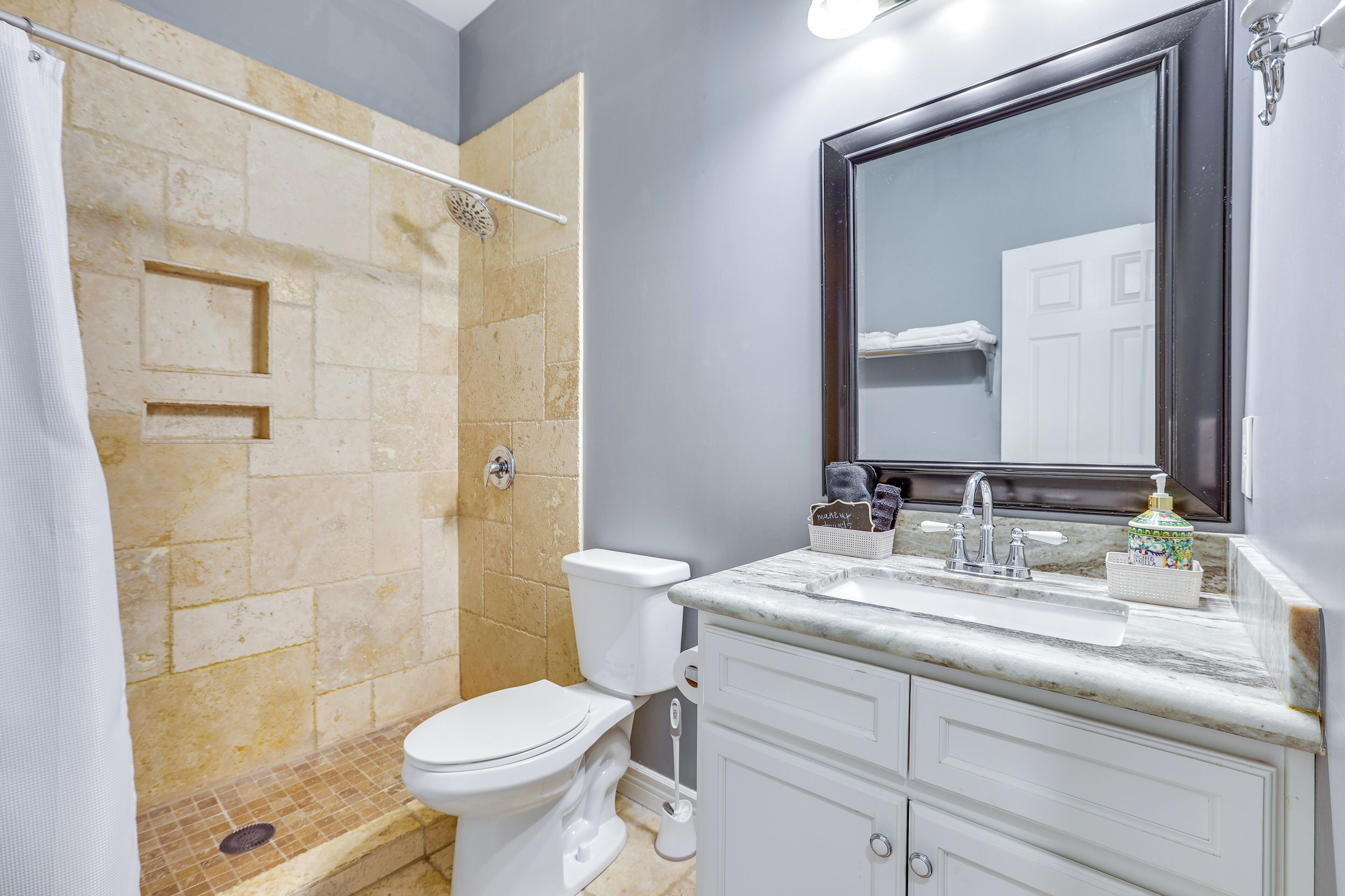 A bathroom with a shower, toilet, sink, and mirror.