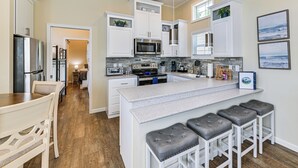 A modern kitchen with white cabinetry, a central island with bar stools, a microwave, and a stove.